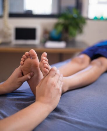 Boy lying on bed while receiving foot massage from female therapist at hospital ward