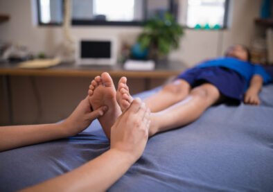 Boy lying on bed while receiving foot massage from female therapist at hospital ward