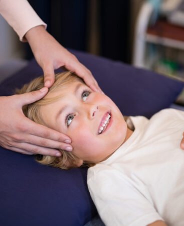 Cropped hands of female therapist giving head massage to boy lying on bed at hospital ward