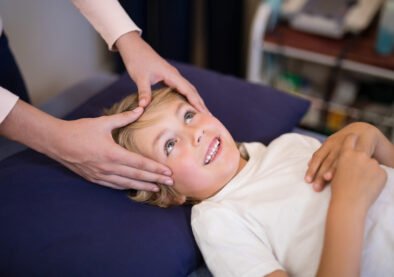 Cropped hands of female therapist giving head massage to boy lying on bed at hospital ward
