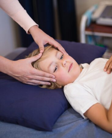 Female therapist massaging head of boy lying on bed at hospital ward