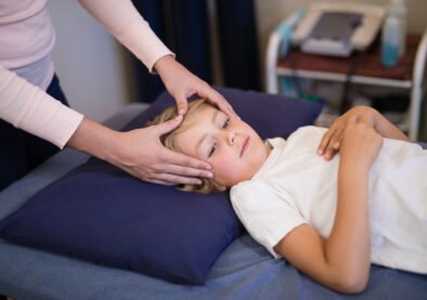 Female therapist massaging head of boy lying on bed at hospital ward